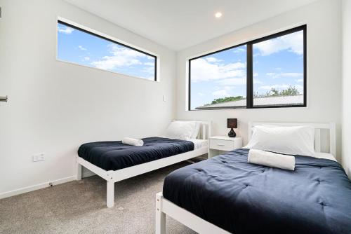 two beds in a room with two windows at Te Atatu Cozy Brand New House 4 in Auckland