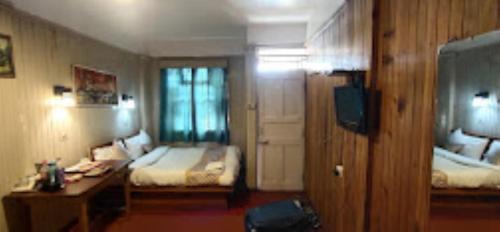 a bedroom with two beds and a desk and a television at Hotel Aliment Darjeeling in Darjeeling