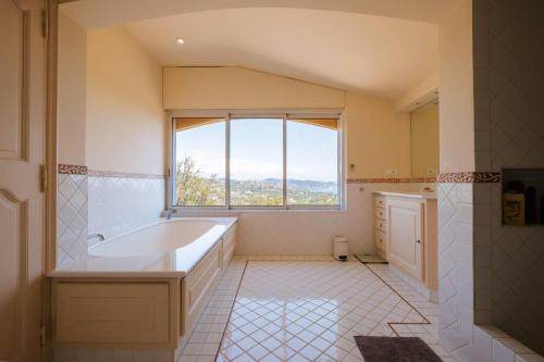 een badkamer met een groot bad en een raam bij La Villa des Cades avec vue mer et piscine privée sur les hauteurs de Stre-Maxime in La Nartelle