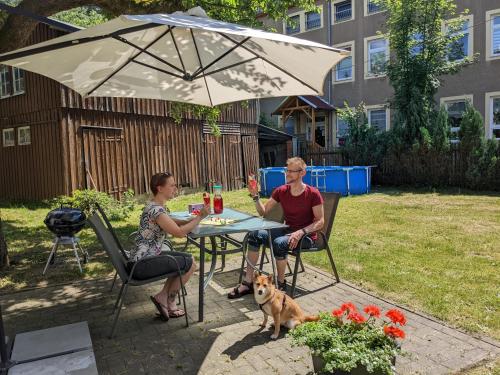 zwei Personen, die mit einem Hund an einem Tisch unter einem Schirm sitzen in der Unterkunft Urlaubsmagie - Wohlfühloase mit Pool - H5 in Sebnitz