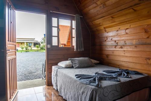 a bed in a wooden cabin with a large window at Chalés Carrara in Alto Paraíso de Goiás