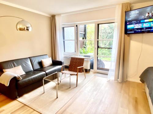 a living room with a black leather couch and a tv at Snug Stays 2 - Design 1-Zimmer-Studio am See mit Terrasse, Garten, Badestelle vor dem Haus in Wörthsee