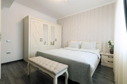 a white bedroom with a large bed and a bench at Olivia Home in Oradea