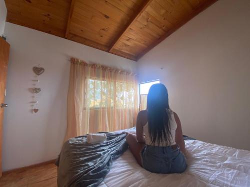une femme assise sur un lit donnant sur une fenêtre dans l'établissement Habitación Matrimonial en Totoralillo Glamping, à Totoralillo