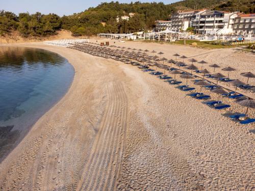 ein Strand mit Sonnenschirmen und Stühlen und das Wasser in der Unterkunft Trypiti Resort Blue Dream Palace and Hive Water Park in Limenaria