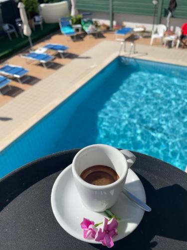 a cup of coffee sitting on a table next to a pool at Hotel Apogeo - Breakfast Experience in Rimini