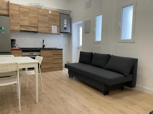 a living room with a black couch and a kitchen at U1 Ap Nuevo, bien comunicado Madrid centro in Madrid
