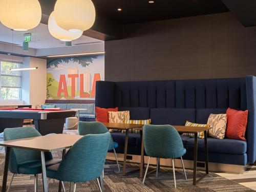 a blue couch in a waiting room with tables and chairs at Tru By Hilton Atlanta Airport College Park in Atlanta