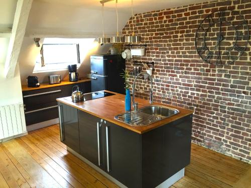 - une cuisine avec un évier et un mur en briques dans l'établissement Le Loft du Clocheton, à Étretat