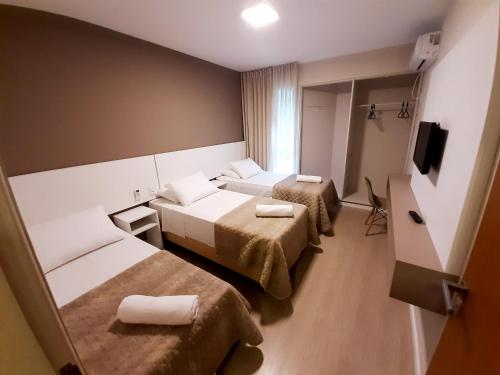 a hotel room with two beds and a television at Caravaggio Praia Hotel in Florianópolis