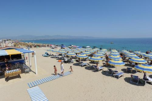 una spiaggia con tanti ombrelloni blu e bianchi e gente di Hotel Poseidon a Corigliano Calabro