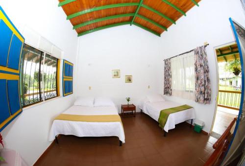 2 camas en una habitación con paredes y ventanas blancas en Finca Hotel Betulia, en La Tebaida