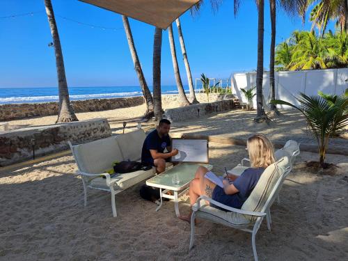 two people sitting at a table with a laptop on the beach at Sunset Surf Villa in La Libertad