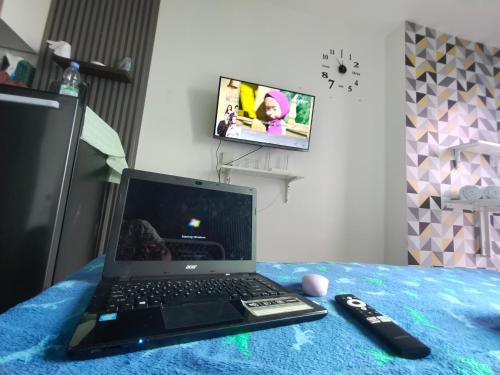 un ordenador portátil sentado en una cama con mando a distancia en Studio Healing at Sayana Apartemen Harapan Indah Bekasi, 