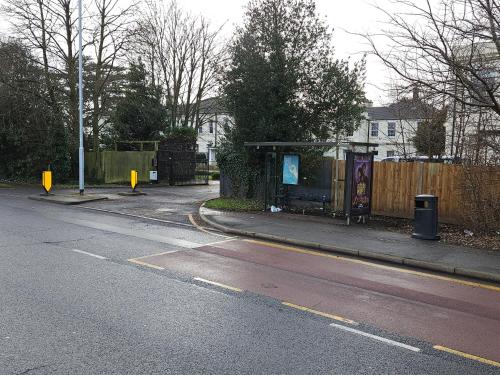 an empty street with a bus stop next to a fence at HEATHROW MANSION SHUTTLES in Uxbridge