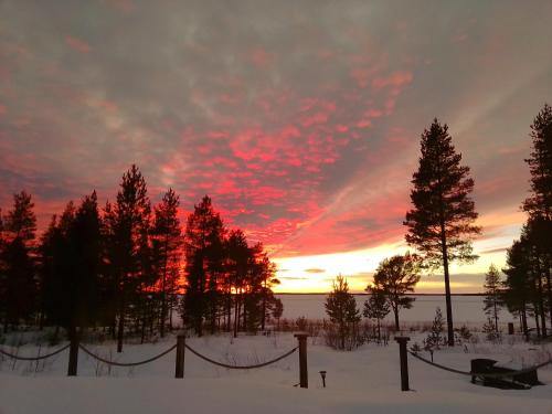 a sunset over a snowy field with trees and a fence at Havsnära villa in Nordmaling