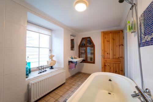 een badkamer met een bad, een raam en een wastafel bij Brosnan's Cottage in Dingle