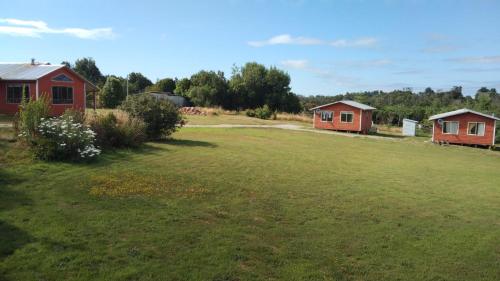 un patio con dos casas rojas y un campo de hierba en Cabañas Rayen Ancud en Ancud