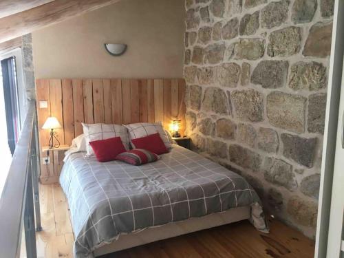 ein Schlafzimmer mit einer Steinmauer und einem Bett mit roten Kissen in der Unterkunft Gîte de charme Le Havre de Paix d'Arcelet in Le Chambon-sur-Lignon
