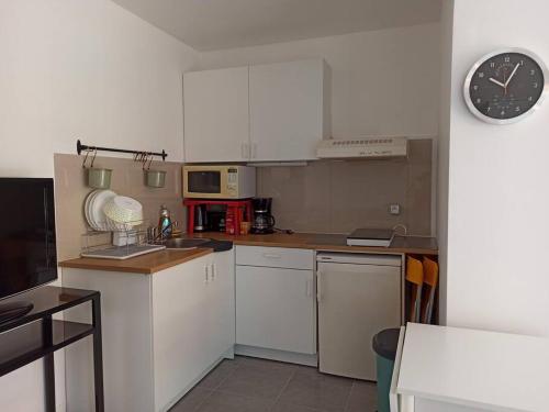 a kitchen with white cabinets and a clock on the wall at Studio 4 pers, terrasse, clim, parking privé inclus in Cannes