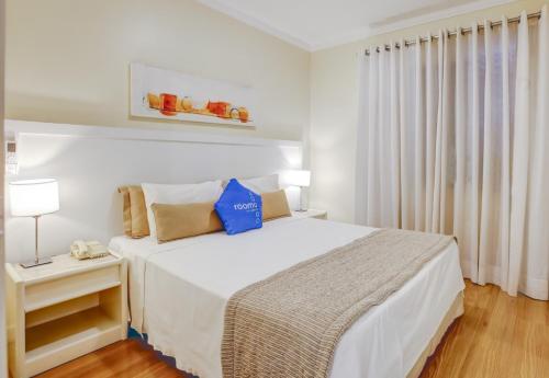 a white bedroom with a large bed with blue pillows at Roomo Residencial Itaim Bibi by Transamérica in São Paulo