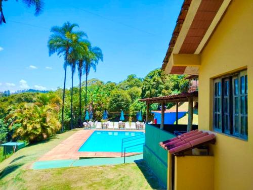 a house with a swimming pool and palm trees at Pousada Recanto do Chalé Ltda in Macacos