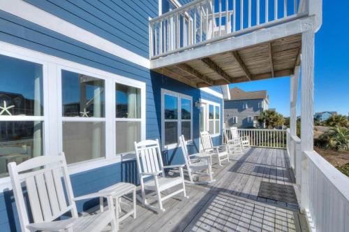 a deck with white chairs on a blue house at A-Frameable Moment in Oak Island