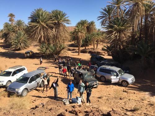 a group of people standing around their cars in the desert at berber desert home for rent in Merzouga