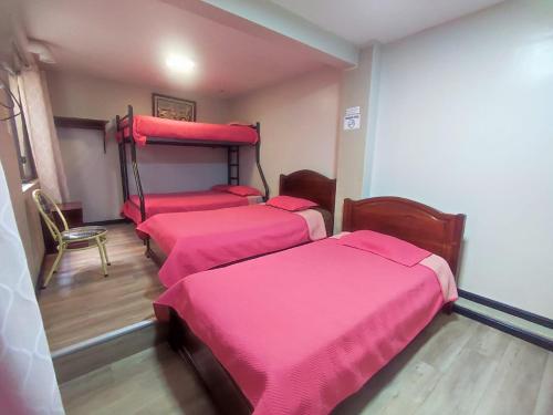 een kamer met 4 bedden met roze dekens en een stoel bij alborada cuenca hospedaje in Cuenca