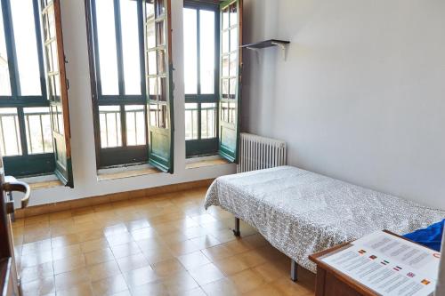 a room with a bed and a table and windows at Albergue Seminario Menor in Santiago de Compostela