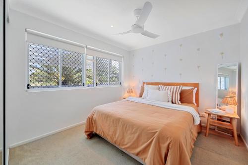 a white bedroom with a bed and two windows at Ohana Vibe Bargara in Bargara