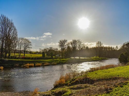 une rivière dans un champ avec le soleil dans le ciel dans l'établissement Fell Cottage, à Oakworth