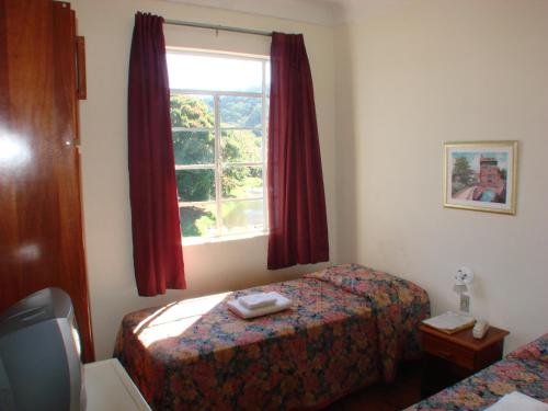 1 dormitorio con 2 camas y una ventana con cortinas rojas en Casa da Ponte Hotel, en Goiás