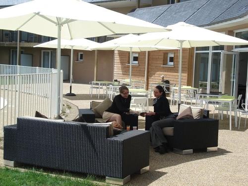 two women sitting on chairs under umbrellas in a patio at Adonis Hauts De Honfleur in Équemauville