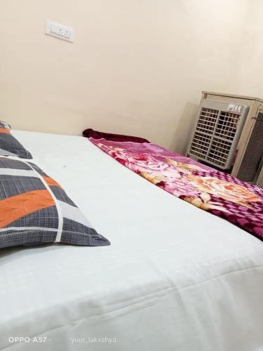 Cama blanca con almohada floral y radiador en MAA HARSIDDHI HOMESTAY, en Ujjain