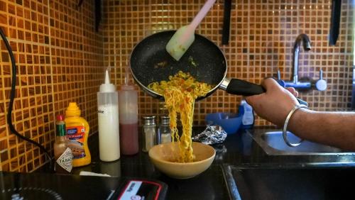 a person is cooking food in a pan in a kitchen at Sortby Stays, Vagator in Vagator