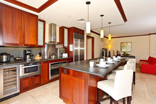 a kitchen with wooden cabinets and a large island with white chairs at Ko Olina Beach Villas B204 in Kapolei