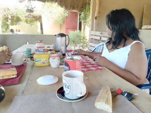 Eine Frau, die an einem Tisch sitzt, mit einem Sandwich und Kaffee. in der Unterkunft assoukatene lodge in Cap Skirring