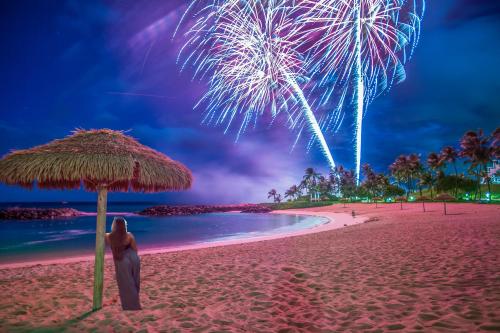 a person standing under an umbrella on a beach with fireworks at Ko Olina Beach Villas O1004 in Kapolei