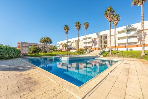 a swimming pool with palm trees in front of a building at GuestReady - Oasis Retreat in Tróia in Troia