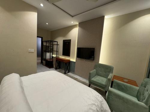 a bedroom with a bed and two chairs and a television at Shelton Boulevard Hotel Lahore in Lahore