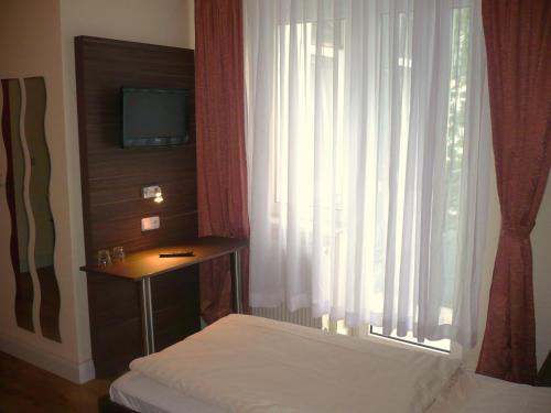 a bedroom with a bed and a window with a television at Hotel Ariana in Cologne