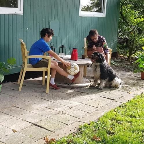 Um par de miúdos sentados numa mesa com um cão. em Huisje de Bosrand em Bant