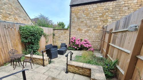 a patio with chairs and a fence and flowers at Bumble Cottage in Chipping Campden