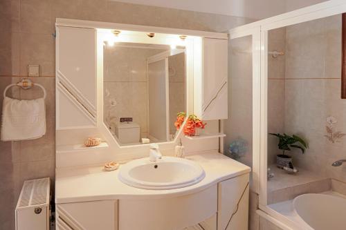 Baño blanco con lavabo y espejo en Villa Sea View Gem Steps to Zia Square Hot Tub, en Lagoúdi Zía