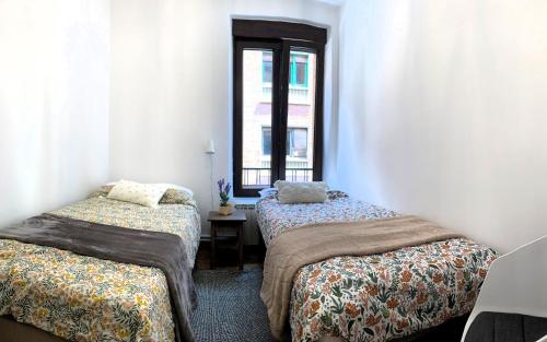 two beds in a room with a window at Bonito piso a 500m de la Catedral in León
