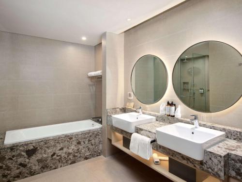 uma casa de banho com 2 lavatórios, uma banheira e espelhos em Mercure Bengkulu em Bengkulu