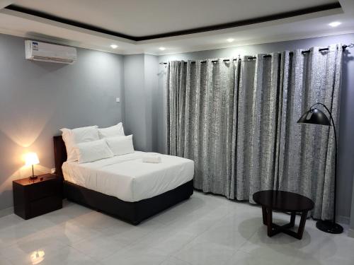 ChipataにあるThe KWASU Apartmentsのベッドルーム(ベッド1台、テーブル、カーテン付)