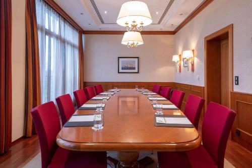 a conference room with a long table and red chairs at ATLANTIC Hotel Wilhelmshaven in Wilhelmshaven