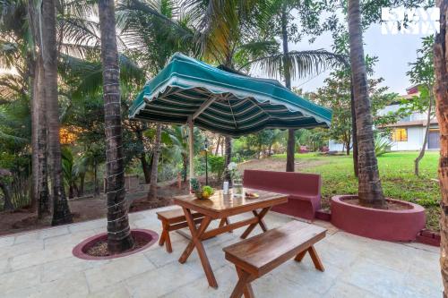 a wooden table and bench with a blue umbrella at StayVista's Firefly Mountain Retreat - Villa with Private Pool, Gazebo & Terrace in Karjat